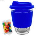 A royal blue glass coffee cup with a silicone lid and sleeve, accompanied by a packet of colourful jelly beans.