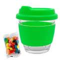 A glass coffee cup with a bright green silicone lid and sleeve, alongside a pack of colourful jelly beans.