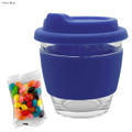 A reusable coffee cup with a navy blue silicone sleeve and lid, accompanied by a packet of colourful jelly beans.