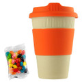 A reusable 12oz bamboo coffee cup in cream and orange, accompanied by a bag of colourful jelly beans.