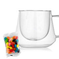 A clear coffee cup with a unique diamond shape alongside a packet of colourful jelly beans.
