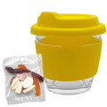A clear glass coffee cup with a yellow silicone lid and sleeve, accompanied by a bag of mixed lollies.