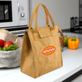 A brown lunch bag with handles, featuring a logo, placed on a countertop among fresh vegetables.