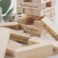 A wooden Small Jenga set with light-coloured blocks, featuring engraved branding on some pieces, scattered on a surface.