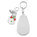 A white pill cutter with a keychain attachment, featuring an open compartment with green and red pills inside.