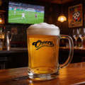 A glass beer mug with a handle, filled with golden beer and topped with frothy white foam, featuring a logo.