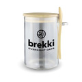 A clear overnight oats container with a wooden lid and spoon, featuring a logo on the side.