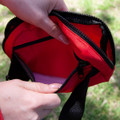 A red bum bag with a zippered opening, showcasing its inner pocket and fabric details. Contains a logo.