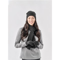 A woman wearing a black knit beanie, long black scarf, and grey long-sleeve top, smiling against a plain background.