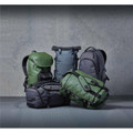 Five backpacks in various shades of green and grey, featuring different styles and designs, with logos visible.