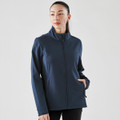 A woman wearing a navy softshell jacket with a high collar and side pockets, featuring a logo on the sleeve.