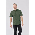 A man wearing a short-sleeved, dark green button-up shirt with a logo, paired with black pants.