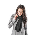 A woman wearing a dark grey scarf, featuring a soft knit texture, paired with a light grey top.