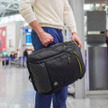 A person holding a black backpack with green accents, featuring a logo, in an airport setting.
