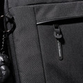 A black laptop sleeve with a zippered pocket and a branded tag. Features a keychain accessory attached.
