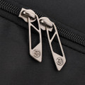Close-up of a black backpack zipper featuring metallic, geometric pull tabs. The fabric has a textured finish.