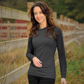 A woman wearing a long-sleeve black t-shirt, walking along a rustic wooden fence with greenery in the background.