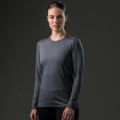 A woman wearing a long-sleeve grey t-shirt stands against a dark background. The shirt features a logo.