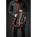 A black and red backpack is held by a person wearing a black jacket, featuring a side pocket for a drink bottle.