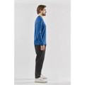 A man models a long-sleeve crew neck shirt in blue, paired with black pants. The shirt features a logo.