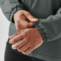 A close-up of hands adjusting the elastic cuff of a dark green thermal jacket, featuring a logo.