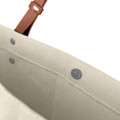A beige cotton tote bag with a leather strap and metal snaps at the top. It features a simple, unbranded design.