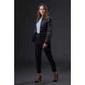 A woman in a black puffer jacket poses against a dark background, wearing tailored black trousers and high heels.