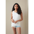 A woman stands wearing a white classic tank top, paired with denim shorts, against a neutral backdrop.