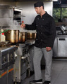 A chef wearing a black chef's cap and black jacket stands in a kitchen with steaming pots.