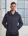A man wearing a navy versatile jacket, standing with hands in pockets against a backdrop of large windows.