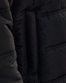 A close-up of a black heavy quilted jacket, highlighting the texture and stitching. The jacket features a brand logo.