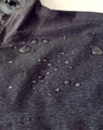 A close-up of a black waterproof performance jacket featuring droplets of water on the surface.