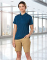 A model wears navy polo and khaki stretch cotton chino shorts in a modern indoor setting. The shorts have a logo.