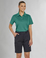 A woman in a teal polo shirt and navy utility cargo shorts, standing confidently with hands in pockets.