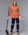 An orange work shirt with reflective stripes, paired with navy pants and work boots, held by a woman with a shovel.