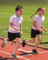 Two children running on a track, wearing white T-shirts and black shorts.