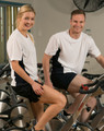 A white and navy short sleeve contrast tee worn by a man and woman sitting on stationary bikes in a gym.