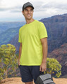 A man wearing a bright yellow short-sleeve performance T-shirt stands against a mountainous backdrop, holding a bag.