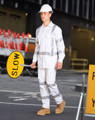 A man wearing a white safety shirt and trousers with reflective stripes holds a 'SLOW' sign. He wears a safety helmet.