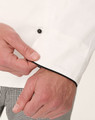 A close-up of a white executive chef jacket featuring black piping, highlighting the cuff detail and button.