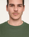 A close-up of a person wearing a green unisex crew neck sweater with a logo on the chest.