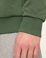 A close-up of a hand wearing a green unisex crew neck sweater, showcasing the ribbed cuff detail.