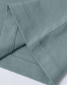 A close-up of a light green premium cotton T-shirt, highlighting the sleeve and stitching details. The shirt has a logo.