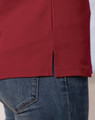 A close-up of a red short sleeve polo shirt featuring side slits, paired with denim jeans. The shirt has a logo.