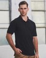A man in a black polo shirt stands against an industrial background, featuring short sleeves and a standard collar.