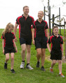 A group of four people wearing matching black and red Men's Alliance polo shirts and shorts, walking on grass.