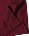 A close-up of the hem and fabric of a burgundy polo shirt, featuring a logo on one side.