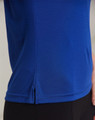 A close-up of a textured polo shirt in vibrant blue, featuring a small slit detail at the hem and a logo.