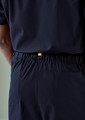 Navy unisex scrub pants with an elastic waistband and a back pocket, featuring a branding tag.