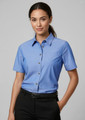 A short-sleeve chambray button-up shirt in blue with a chest pocket, modelled by a woman.